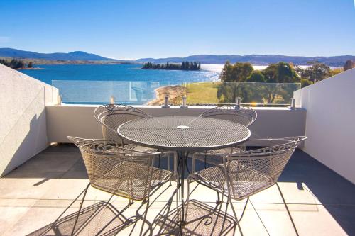 a table and chairs on a balcony with a view of the water at Horizons Lake Jindabyne in Jindabyne