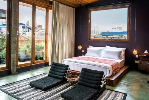 a bedroom with a bed and two chairs and windows at Ba Hao Residence in Bangkok