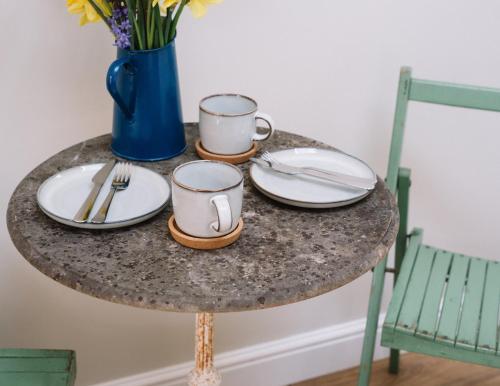 a table with two cups and plates and a vase of flowers at Field View Lodge in Niton