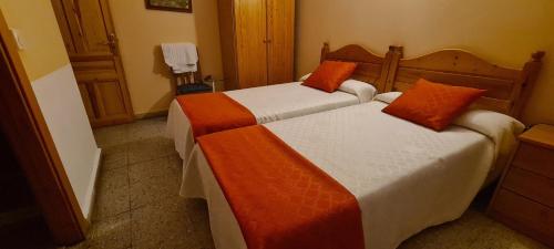 2 Betten mit orangefarbener und weißer Bettwäsche in einem Zimmer in der Unterkunft Hostal de la Playa in Barro de Llanes