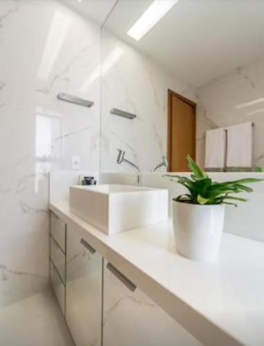a white bathroom with two sinks and a potted plant at Bangalo Malawi em Muro Alto PE in Porto De Galinhas