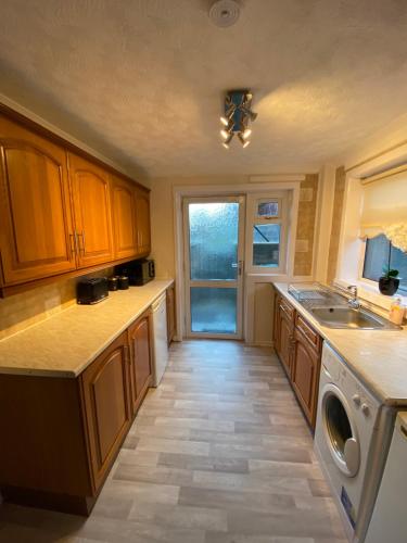 a large kitchen with wooden cabinets and a window at Dunfermline, 2 bedroom home free on street parking in Fife