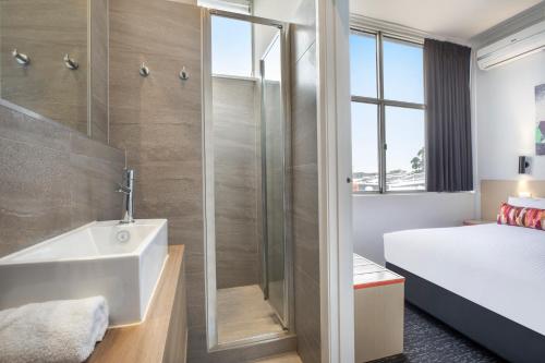 a bathroom with a shower and a sink and a bed at Nightcap at Ashley Hotel in Braybrook