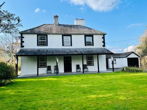 a white house with chairs on a green lawn at Aberhiriaeth Hall - Country House By River Dyfi in Cemmaes