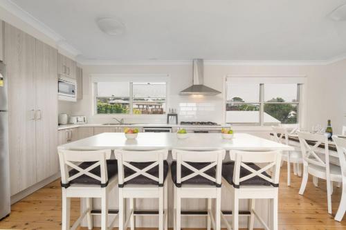 a white kitchen with a large white island with bar stools at Villa Killara by Experience Jervis Bay in Vincentia