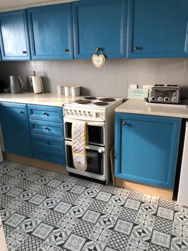 ポートラッシュにあるRoyale Court Apartments Portrushの青いキャビネット、タイルフロアのオーブン付きのキッチンが備わります。