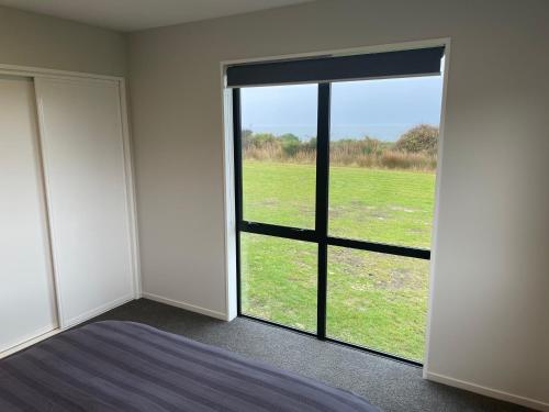 a bedroom with a large window with a view of a field at Toko Mouth Beach House in Glenledi