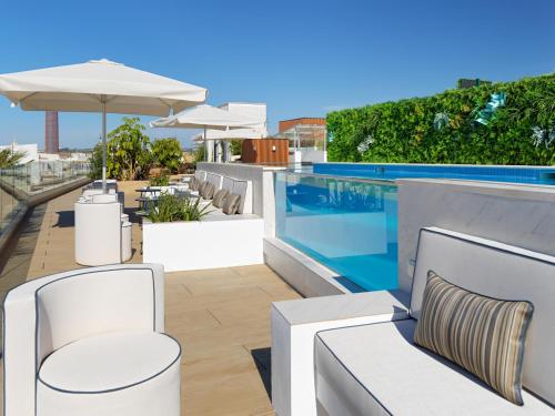 a swimming pool with white chairs and an umbrella at H10 Casa de la Plata in Seville