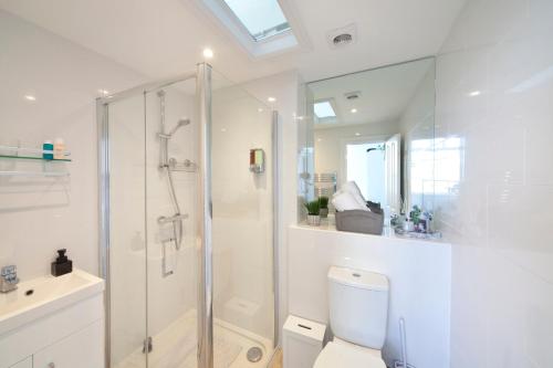 a white bathroom with a shower and a toilet at Beachfront Compact Coastal Crib, DIRECT Sea Views & Air Conditioning in Littlestone-on-Sea