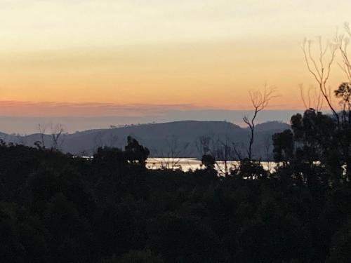 a sunset over a body of water with trees at Winganah Cottage in Murdunna