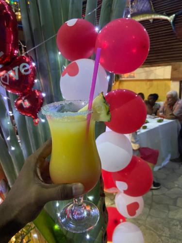 a person holding a drink in front of a bunch of balloons at Hôtel Restaurant Coco Lodge Majunga in Mahajanga