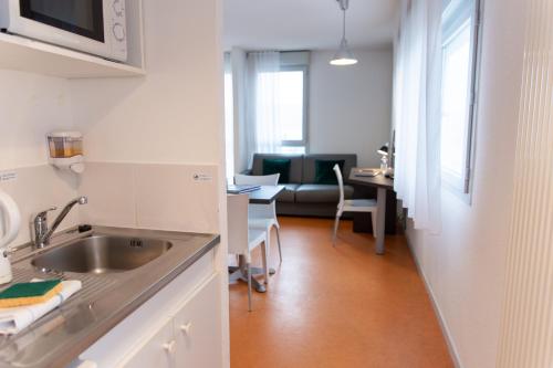 a kitchen with a sink and a living room at Zenitude Hôtel-Résidences Les Hauts Du Chazal in Besançon