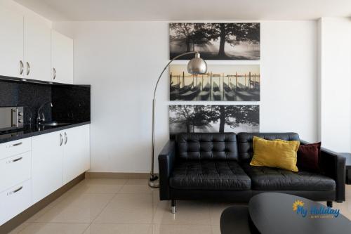 a living room with a black couch and a kitchen at Esther's Sea View in Playa del Ingles