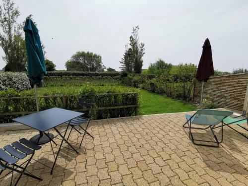 2 Stühle, ein Tisch und 2 Sonnenschirme auf einer Terrasse in der Unterkunft Ty Bian, à la campagne et proche de la plage in Le Conquet
