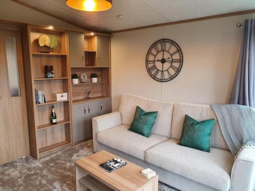 a living room with a couch and a clock on the wall at Beautiful Borders Cabin in Jedburgh