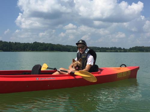 a man and a dog in a red boat on the water at Przystań Piława in Borne Sulinowo