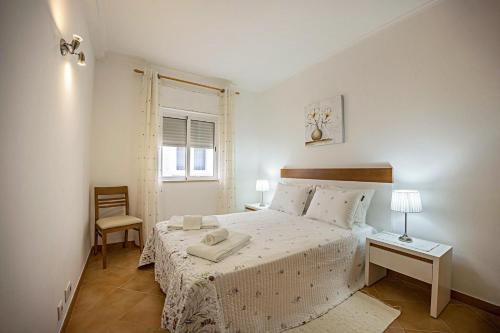 een witte slaapkamer met een bed en een stoel bij Casa Bege T2 in Burgau