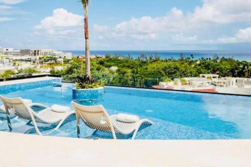 a pool with chairs and a palm tree and the ocean at LOFT VIEW SEA The best ubication at 5th AV in Playa del Carmen