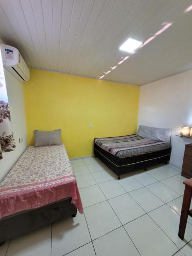 a room with two beds and a yellow wall at Casa do Angelo in Ilha de Boipeba