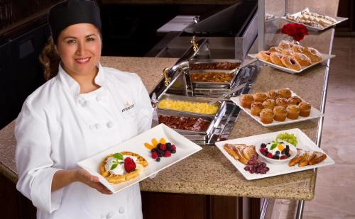 a chef holding two plates of food on a counter at Ayres Hotel Laguna Woods - Aliso Viejo in Laguna Woods