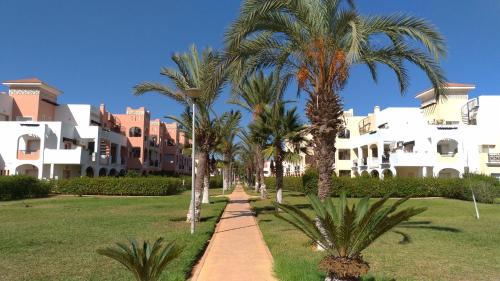 un chemin avec des palmiers devant un bâtiment dans l'établissement Chez Younès Appartement Marina Saidia Ap2, à Saïdia