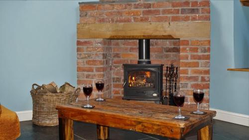 a fireplace with three glasses of wine on a wooden table at Sheep Dip Cottage - 5* Cyfie Farm, with log burner and private hot tub in Llanfyllin