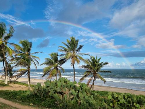 a rainbow over a beach with palm trees and the ocean at Casa (Village) beira mar em Praia do Flamengo in Salvador