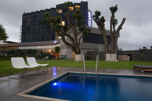 uma piscina com duas cadeiras brancas e um edifício em Park Inn by Radisson Libreville em Libreville