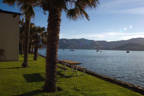 a picnic table next to a lake with palm trees at Akaroa Waterfront Motels in Akaroa