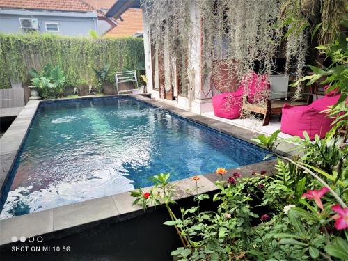 a swimming pool in a garden with pink furniture at G Saskara Homestay in Sanur
