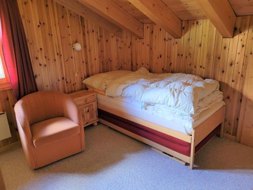a bed and a chair in a room with wooden walls at Ferienwohnung Traumzeit OG/DG in Bellwald