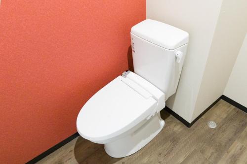 a white toilet in a bathroom with a red wall at ミチ旅ホテル 読谷 in Yomitan