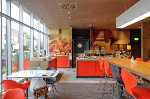 a restaurant with red tables and chairs and a kitchen at ibis Luebeck City in Lübeck