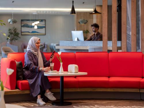 a woman sitting on a red couch with a table at Ibis Jeddah Malik Road in Jeddah