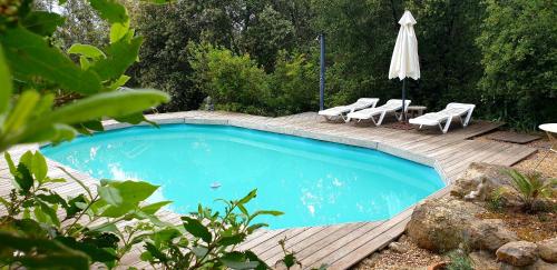 a swimming pool with chairs and an umbrella on a wooden deck at Le Cocon in Vézénobres