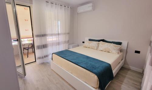 een witte slaapkamer met een bed met een blauwe deken bij Small Studio near the Olimpik Park in Tirana