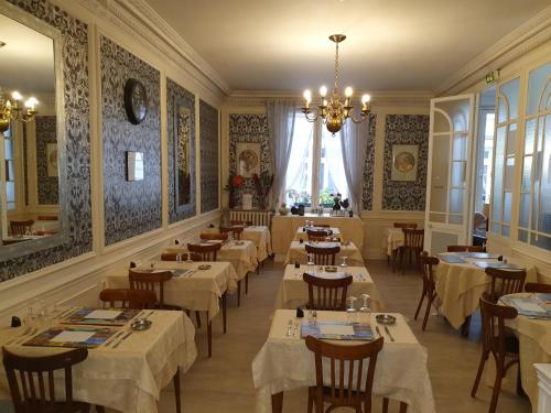un restaurant avec des tables et des chaises blanches et un lustre dans l'établissement Hôtel Riviera, à Vichy