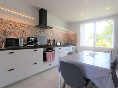 une cuisine avec des armoires blanches, une table et une fenêtre dans l'établissement Maison rénovée 3 étoiles à 150m de la plage, idéale pour familles avec espace enfants et Wifi - FR-1-481-116, à Bénodet