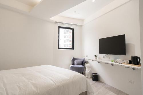 a white bedroom with a bed and a tv on a wall at The Way Inn in Taichung
