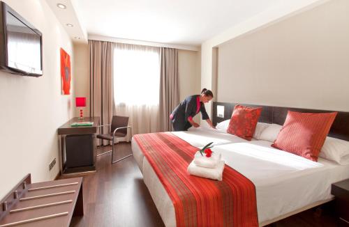 a woman standing next to a bed in a hotel room at Sercotel Aura Algeciras in Algeciras