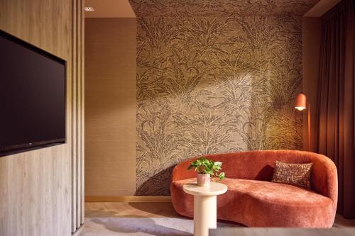 a living room with a orange chair and a tv at Van der Valk Hotel Arnhem in Arnhem