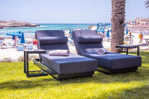 two lounge chairs sitting on the grass near the beach at Pavlo Napa Beach Hotel in Ayia Napa
