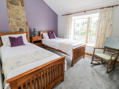 1 dormitorio con 2 camas, silla y ventana en Box Tree Cottage, en Keighley