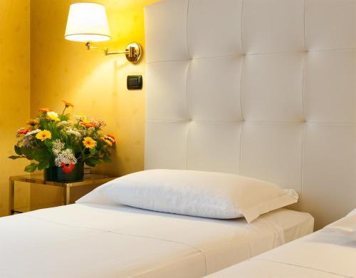a white bed with a pillow and a vase of flowers at Hotel Lombardia in Milan