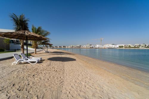 a beach with two chairs and an umbrella and the water at Marbella Luxury 3BR & 5BR Villas at Hayat Island, Mina Al Arab in Ras al Khaimah
