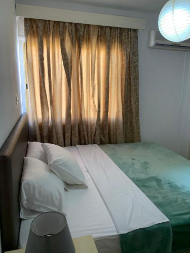 łóżko z poduszkami i okno z zasłoną w obiekcie Green Nondas Hill w Larnace