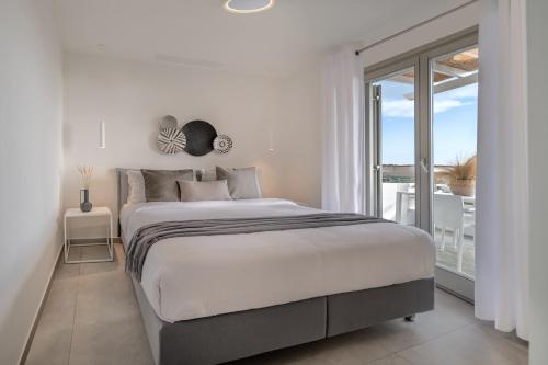 a white bedroom with a bed and a large window at NiMa Sifnos Residences in Apollonia