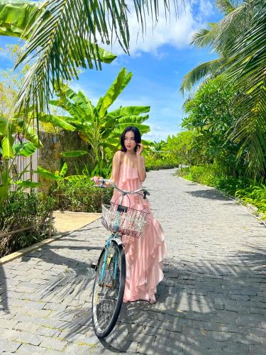 a woman in a pink dress standing next to a bike at Que Toi Village Resort Phu Yen in Song Cau