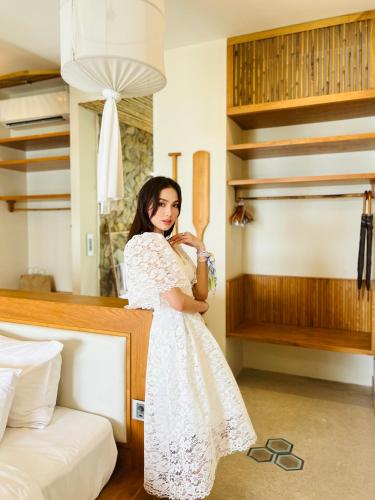 a woman in a white dress standing next to a bed at Que Toi Village Resort Phu Yen in Song Cau