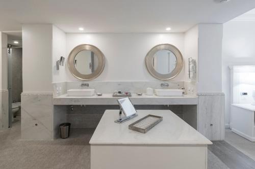 a white bathroom with two sinks and two mirrors at La Mision Hotel Boutique in Asuncion